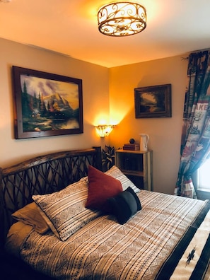 A bed with patterned bedding, a headboard, and a wall-mounted lamp.