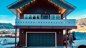 Un rifugio con garage, un balcone decorato con elementi naturali e uno sfondo montuoso.