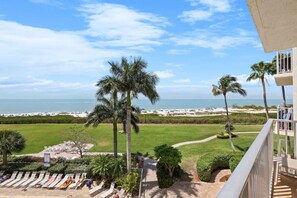 A balcony with a view of the beach, palm trees, and a grassy area with lounge chairs. - Beachfront-Pool-Fort Myers Beach(our Pool is open) (Fort Myers Beach)