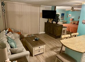 Una sala de estar con sofá, mesa de centro, televisor y un comedor con mesa y sillas.