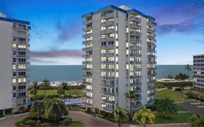A high-rise hotel with multiple balconies, a pool area, and a view of the ocean.