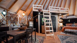 Un interior acogedor con una mesa de madera, una escalera y una cama con un edredón estampado.