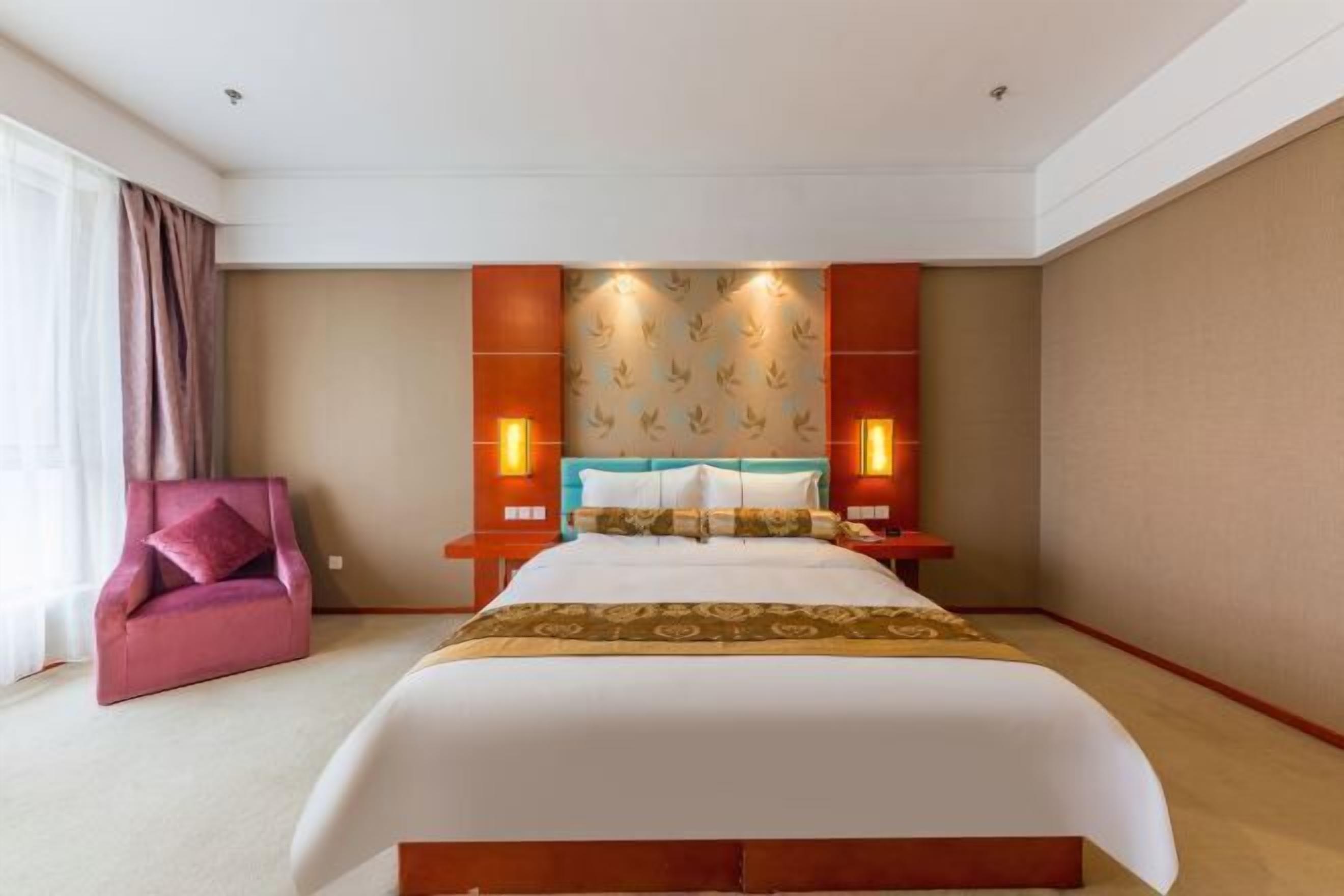 Ett hotellrum med en stor säng, en rosa fåtölj och en sänggavel med ett bladmotiv.