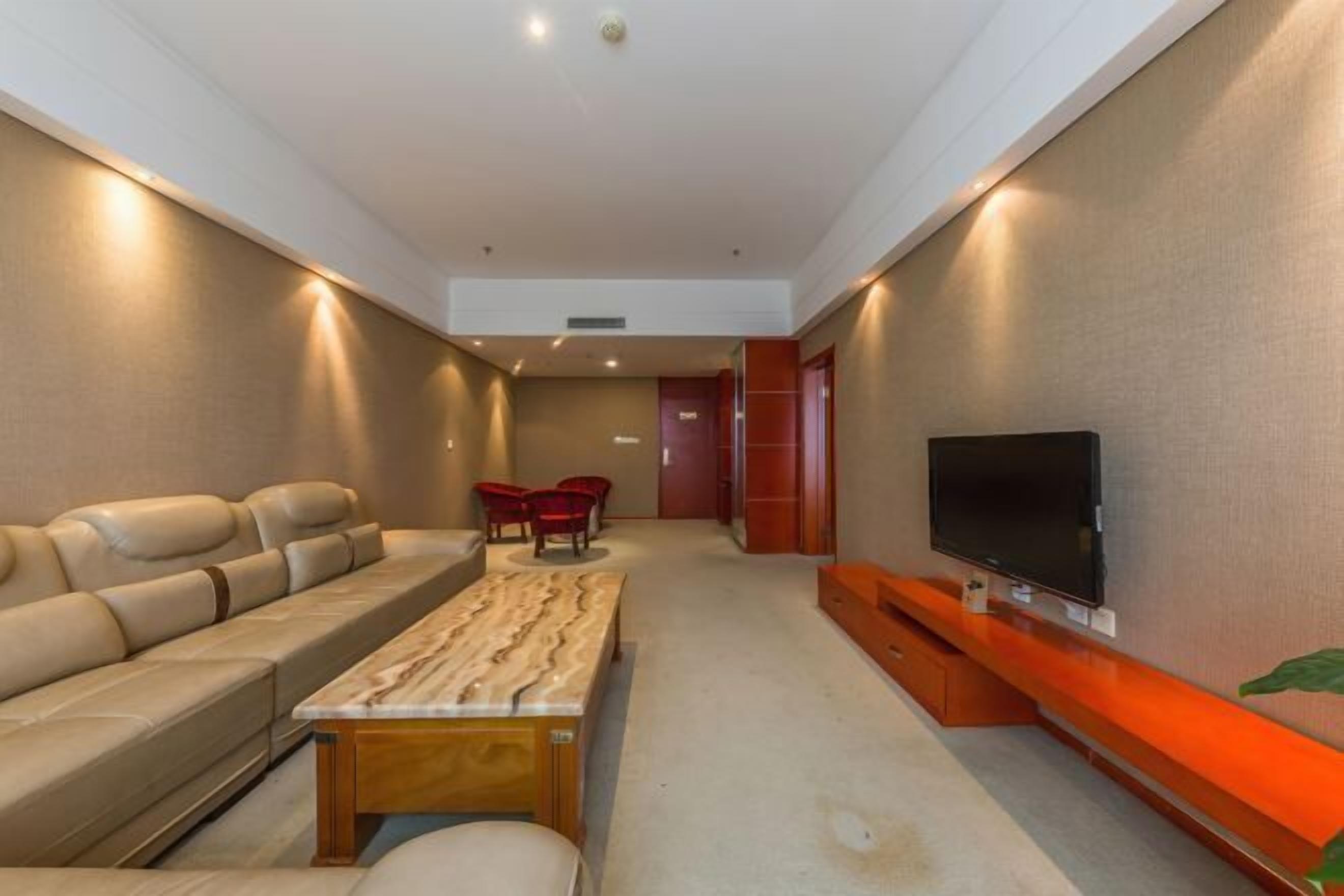 A modern living room with a sofa, a coffee table, red chairs, a TV, and a red accent wall.