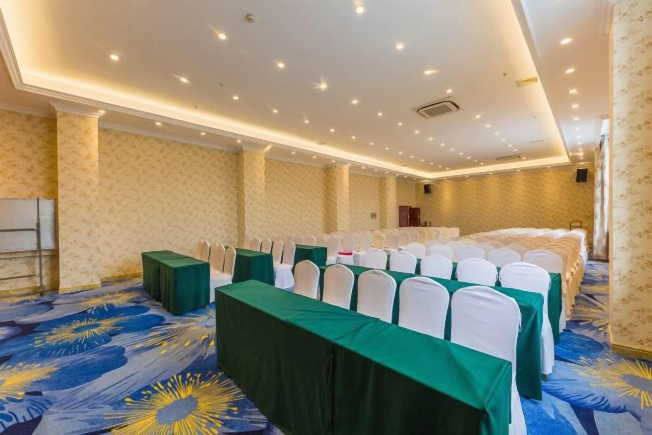A conference room with rows of tables, white chairs, and a patterned carpet.