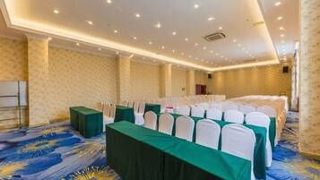 A conference room with rows of tables, white chairs, and a patterned carpet.