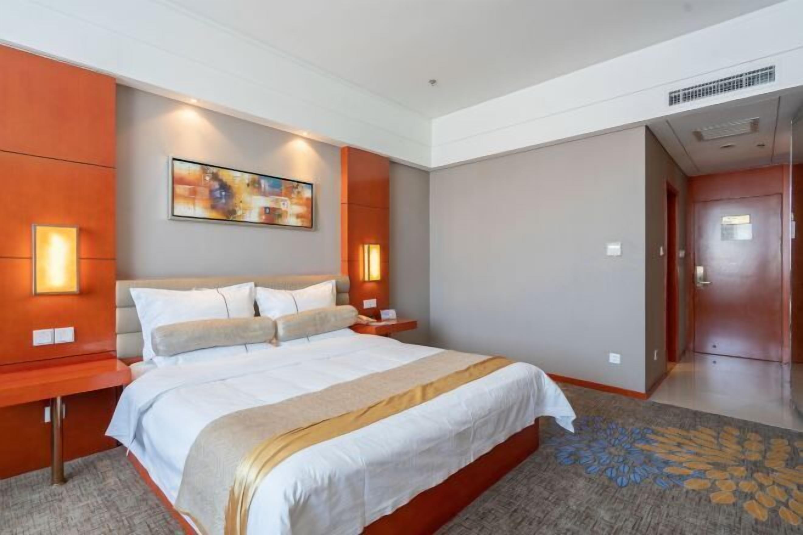 A hotel room with a large bed, two bedside tables, a wall-mounted painting, and a carpeted floor.