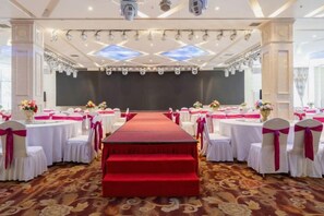 A banquet hall with a central stage, rows of round tables with white tablecloths and pink sashes, and a red carpet leading to the stage. - Dongpeng Holiday Hotel (Hohhot)