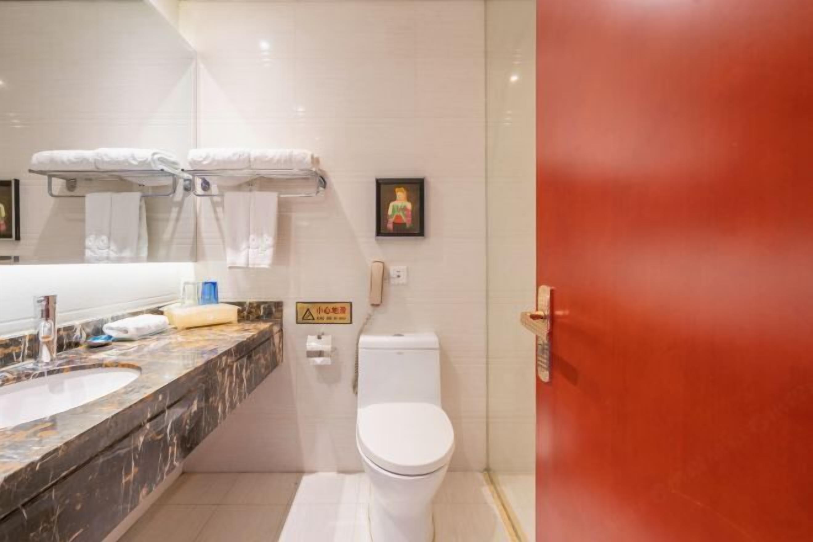 Un baño con lavamanos de mármol, inodoro y puerta roja.