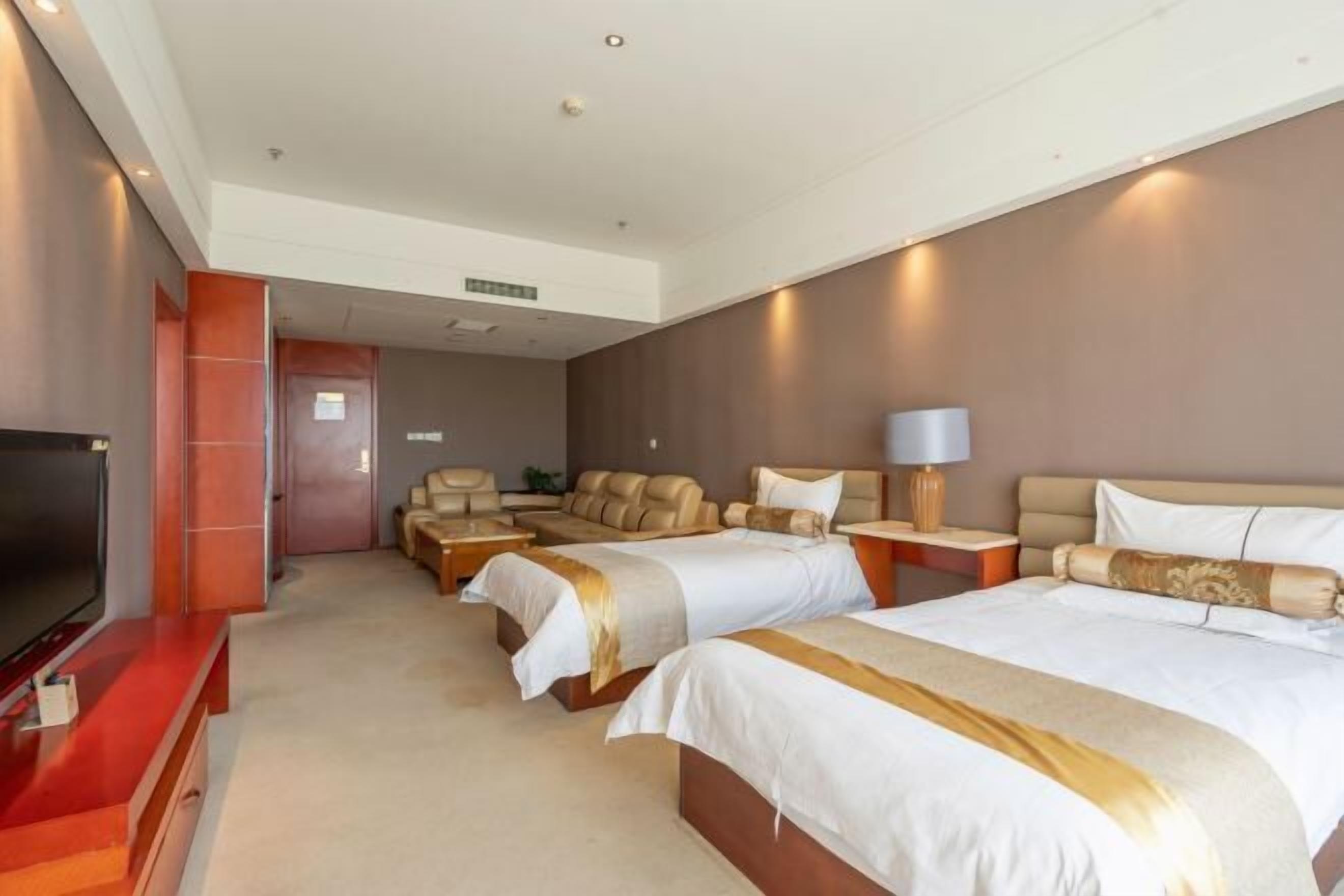 A hotel room with two beds, a TV, a sofa, and a desk with a lamp.