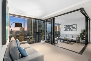 Un salon moderne avec un canapé gris, une table basse et une porte vitrée donnant sur un balcon avec vue sur la ville.
