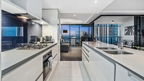 A modern kitchen with a central island, a built-in oven, and a view of the cityscape through large windows. - Circle on Cavill, 2 bed,Pool,Spa (Surfers Paradise)