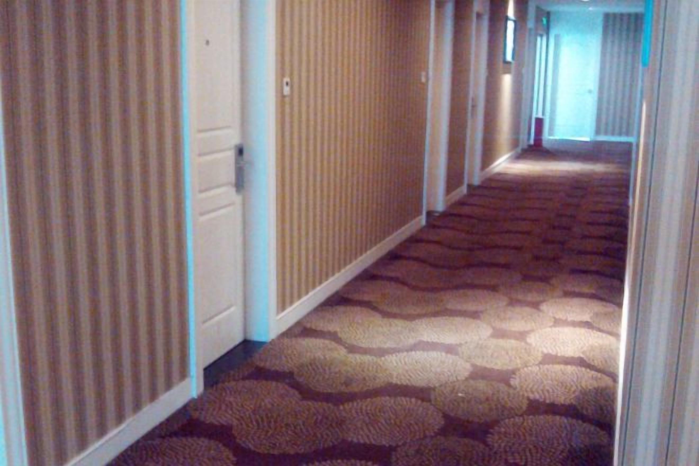 A hotel corridor with patterned carpet, doors, and a view into a room.