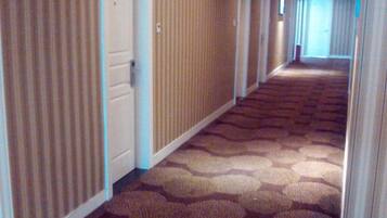 A hotel corridor with patterned carpet, doors, and a view into a room.