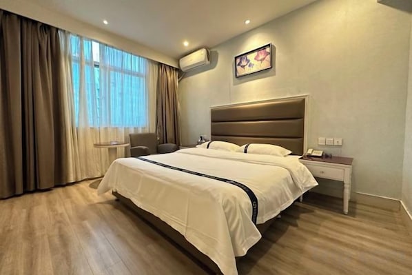 Una habitación de hotel con una cama grande, una mesita de noche, una silla y un ventanal con cortinas.