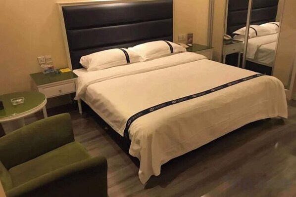 Quarto de hotel com cama, uma cadeira verde, mesa de cabeceira e espelho.