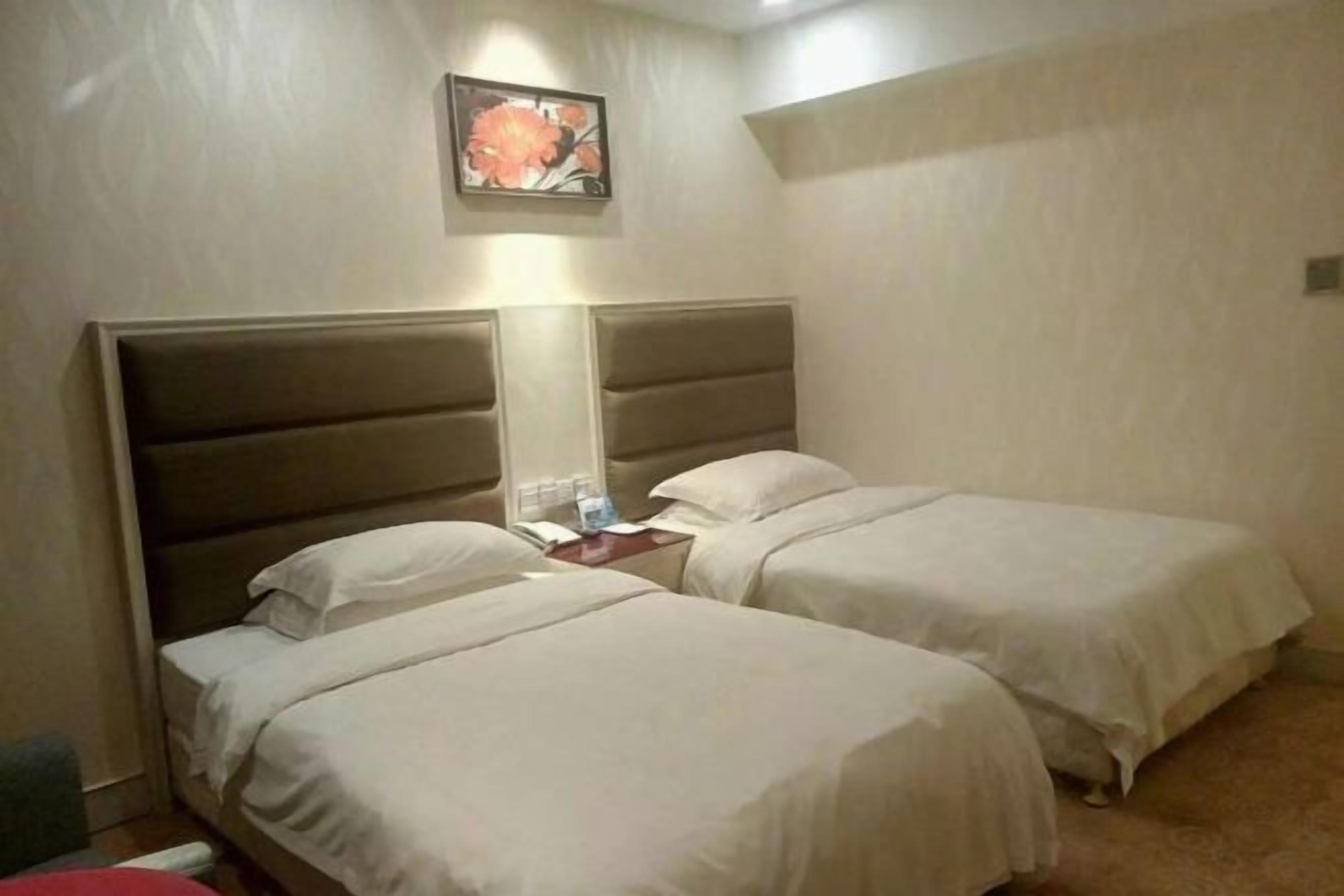 A hotel room with two beds, a nightstand, a lamp, and a framed picture on the wall.