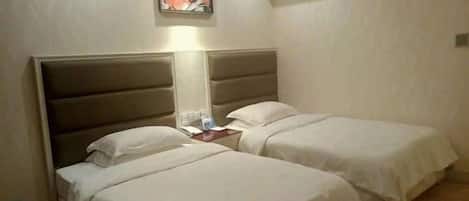 A hotel room with two beds, a nightstand, a lamp, and a framed picture on the wall.