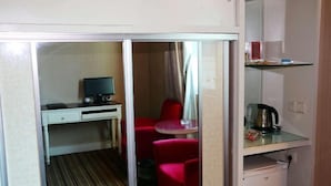 A compact room with a desk, a chair, a small table with a kettle, and a red chair.