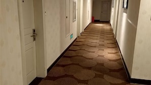 A hotel hallway with doors on both sides, a patterned carpet, and a long corridor.