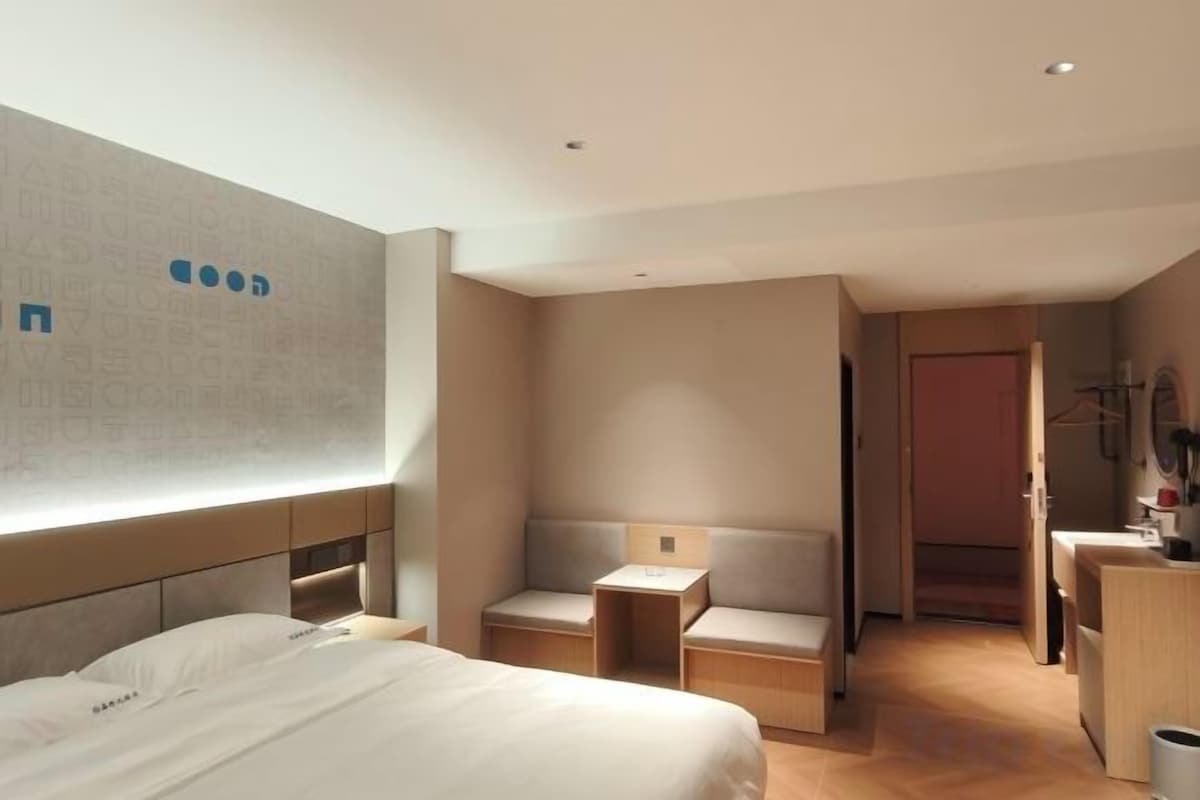 Quarto de hotel moderno com uma cama grande, área de estar, escrivaninha e espelho.