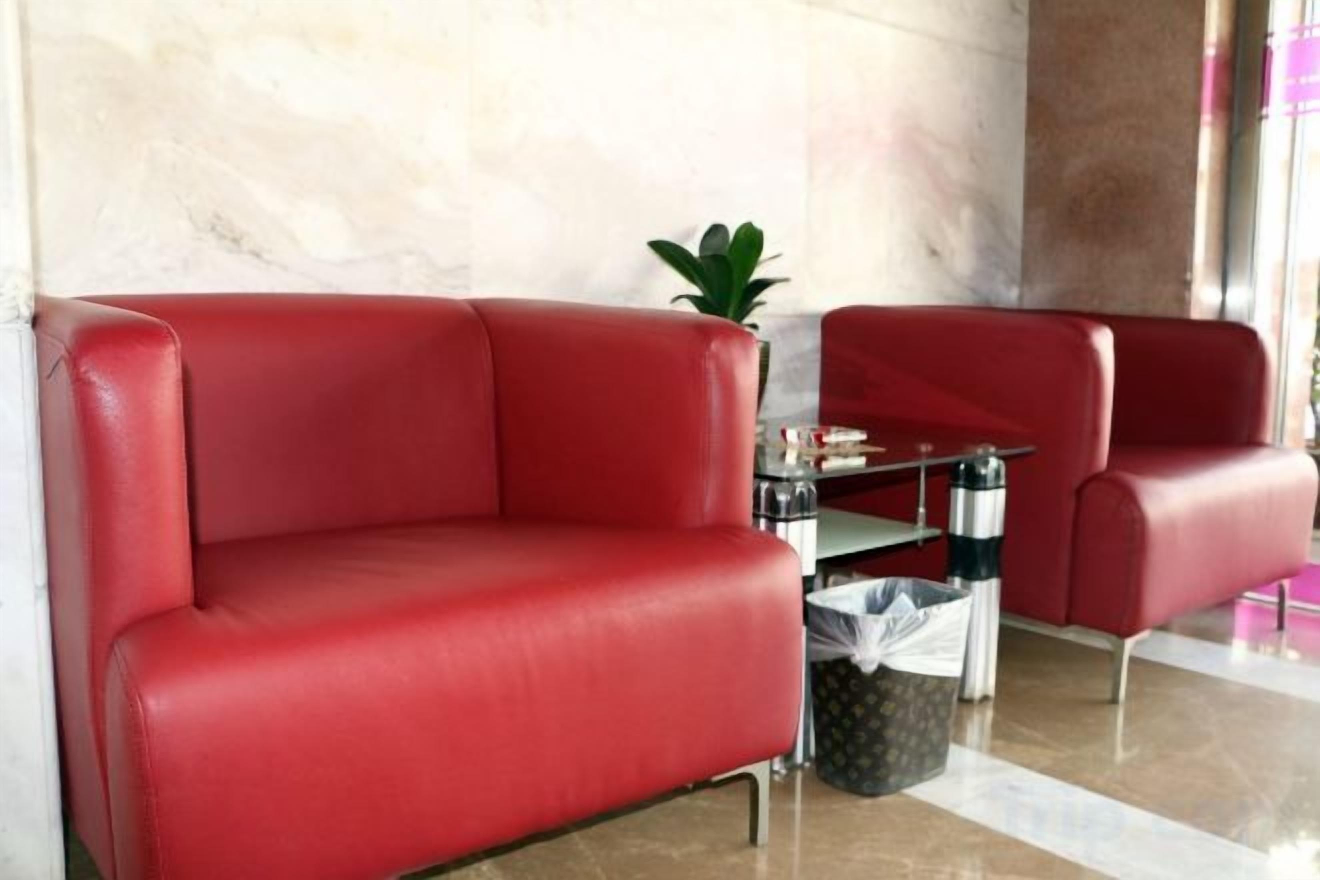 A red leather sofa and armchair in a lobby area with a marble wall and a small table with a plant.