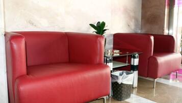 A red leather sofa and armchair in a lobby area with a marble wall and a small table with a plant.