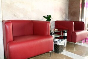 Sofá e poltrona de couro vermelho numa área de recepção, com parede de mármore e uma pequena mesa com uma planta.
