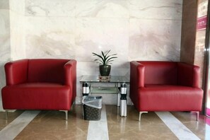 Dos sillones rojos de cuero, una mesa de vidrio con planta en maceta y un cubo de basura.