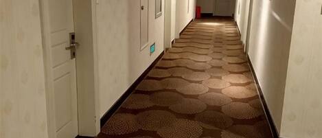 A hotel hallway with doors on both sides, a patterned carpet, and a red object on the floor.