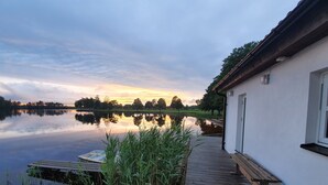 A calm lake with a wooden dock leading to a white building with a window and a door.
