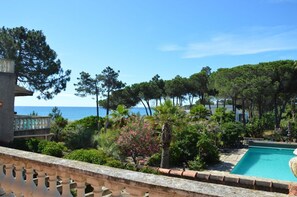 Zona de piscina con vistas al mar, rodeada de vegetación exuberante y un edificio de piedra.
