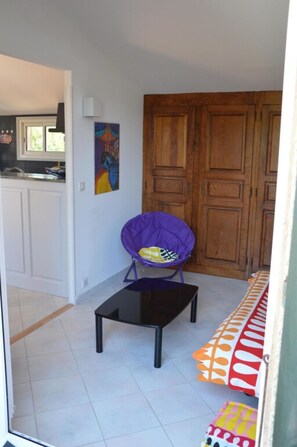 A small, open-plan living space with a kitchen area, a purple chair, a black table, and a colorful sofa.