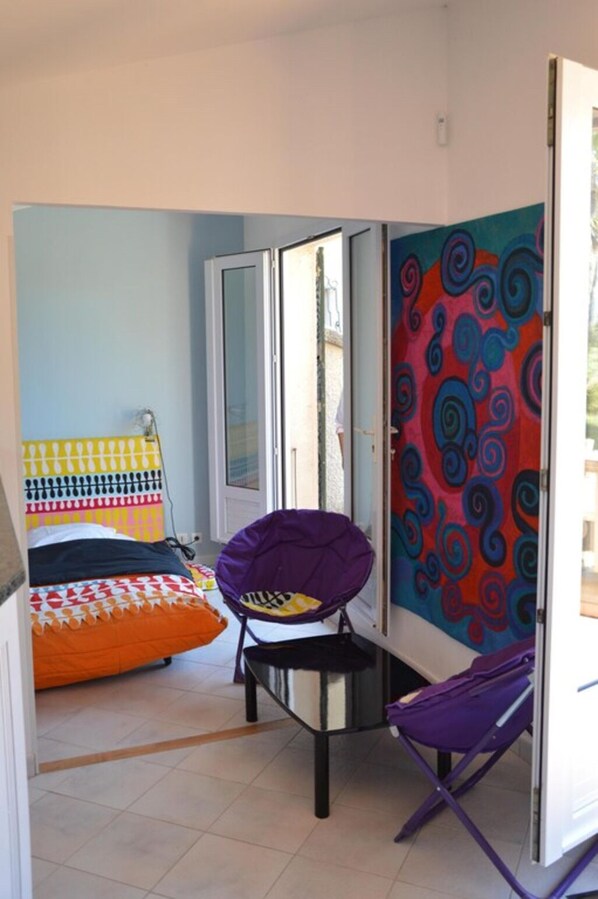 Una habitación con una cama, una silla, un muro colorido y una puerta.
