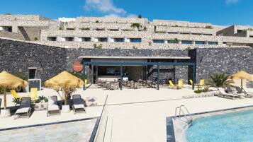 A pool area with lounge chairs and umbrellas, a bar, and a stone wall.
