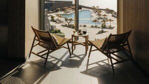 Een balkon met twee rieten stoelen en een kleine tafel, met uitzicht op een zwembadgedeelte met parasols en ligbedden.