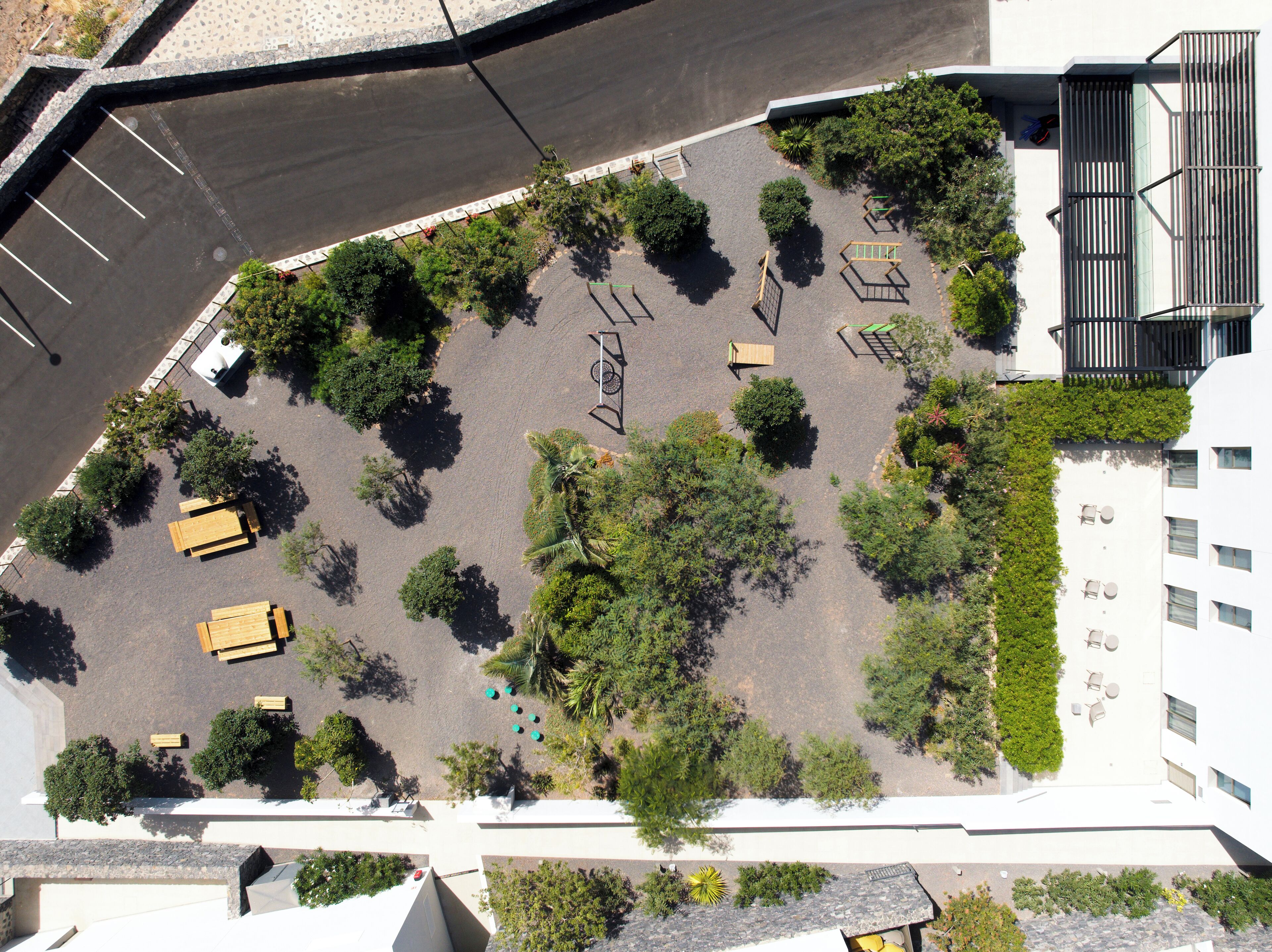 An aerial view of a parking lot with trees, benches, and a building with a balcony.