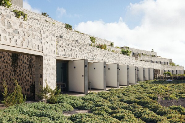 A row of stone buildings with open doorways, surrounded by a landscaped garden.