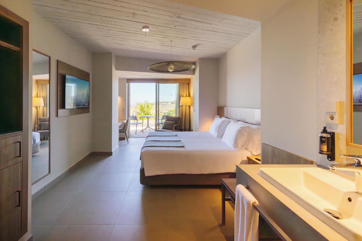A hotel room with a large bed, a bathroom with a sink, and a view of the outdoors.