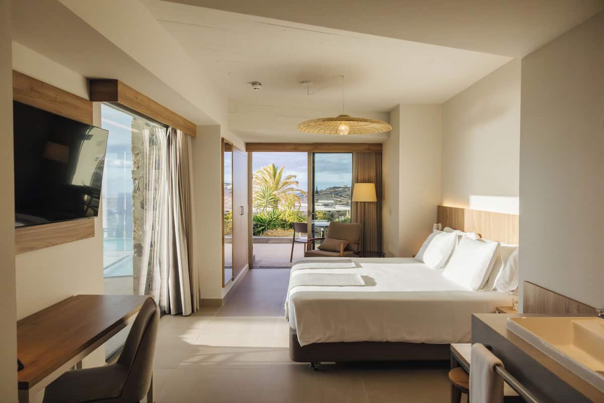 A hotel room with a bed, a desk, a chair, a TV, a lamp, and a bathroom with a bathtub.