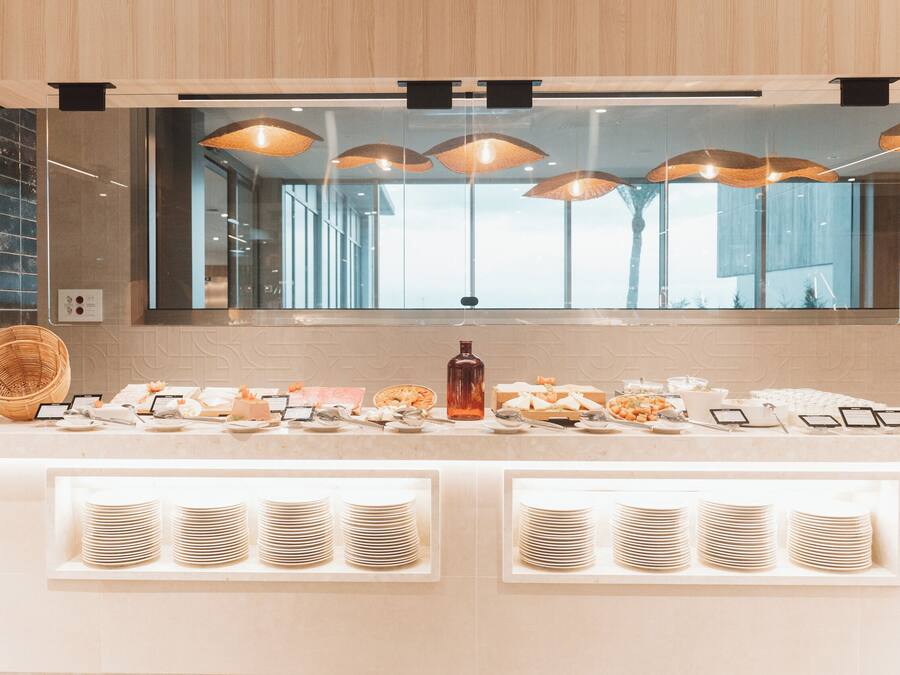 Un buffet allestito con piatti, ciotole e una bottiglia, sotto un ampio specchio con lampade a sospensione.