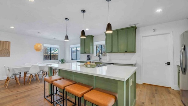 Una cocina moderna con una isla central, armarios verdes e iluminación colgante.