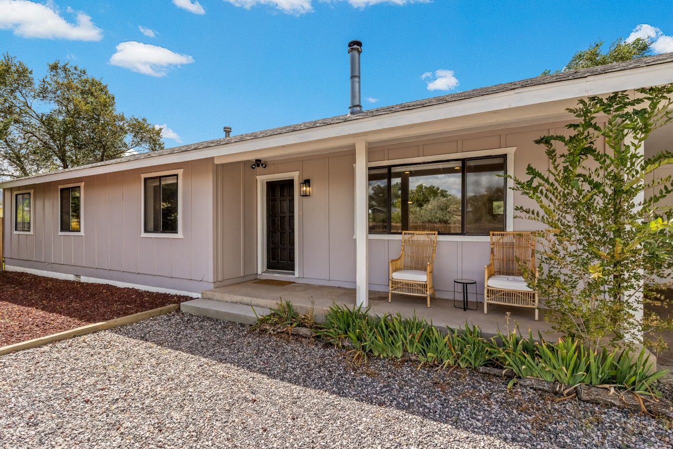 Une maison moderne de plain-pied, dotée d’un porche abrité, de deux fauteuils en osier et d’une petite table.