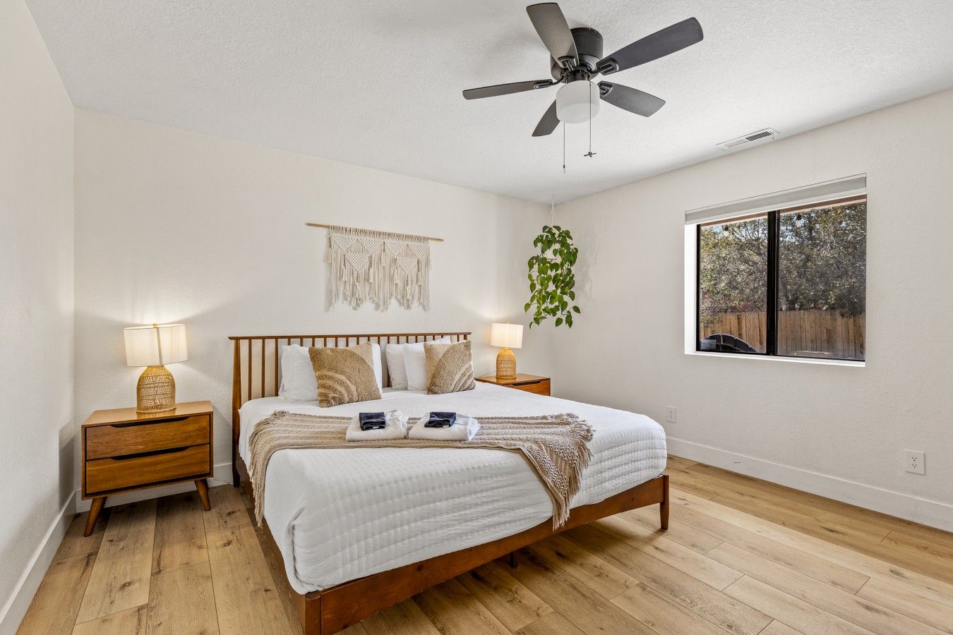 Une chambre à coucher comprenant un lit, des tables de chevet, un ventilateur de plafond, une fenêtre avec vue et une décoration murale en macramé.