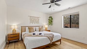 Une chambre à coucher comprenant un lit, des tables de chevet, un ventilateur de plafond, une fenêtre avec vue et une décoration murale en macramé.