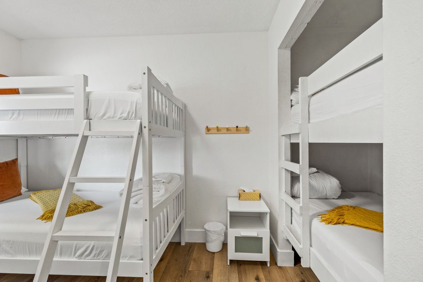 Une chambre avec des lits superposés, une petite table de chevet, une étagère fixée au mur et une poubelle.
