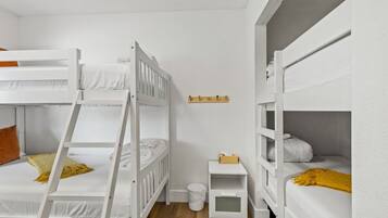 Une chambre avec des lits superposés, une petite table de chevet, une étagère fixée au mur et une poubelle.