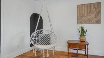 Une pièce avec un fauteuil suspendu, une petite table en bois et une plante en pot.