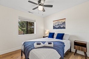 A bedroom with a bed, a ceiling fan, a window, a nightstand, and a wall-mounted artwork. - The Getaway in Williams  (Williams)