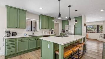 Une cuisine moderne avec des meubles verts, un îlot central blanc doté de tabourets et un éclairage suspendu.